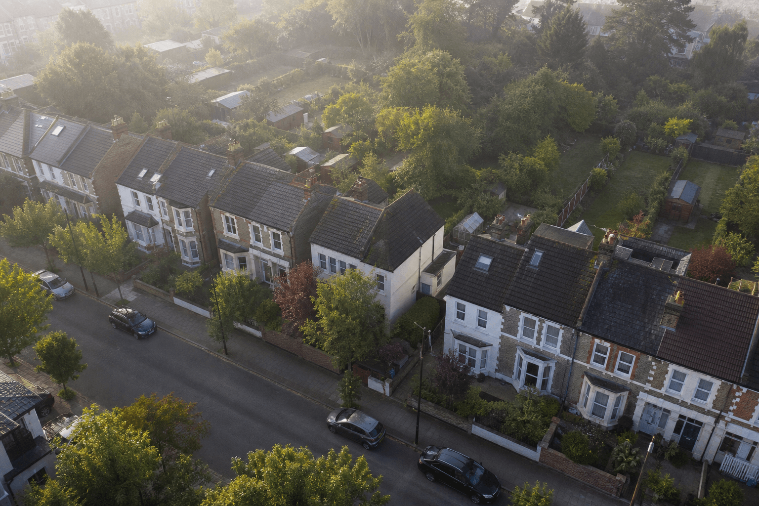 Aerial view of a leafy UK residential street with rows of period semis and terraces in soft morning light.